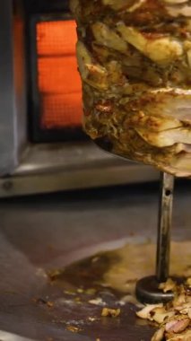 Taze oyulmuş shawarma eti, bir el onu ahşap bir spatulayla alıp ticari mutfakta bir tepsiye koyarken dönüşümlü tükürükten düşer..