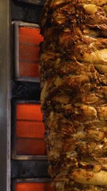 Kıtır kıtır, terbiye edilmiş shawarma etinin arka planda parlayan ısı elementleriyle birlikte dikey bir rostoda kızarmasının ayrıntılı görüntüsü..