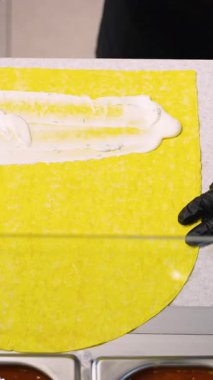 Şavurma ambalajlarını, taze malzemelerle birlikte yiyecek reyonundaki sarı ekmek üzerinde öğütülmüş sebzelerle birleştiren ellerin yakın çekimi..