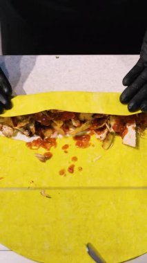 Elleri plastik eldivenle sarmalayan shawarma dürümleri fast food tezgahında taze sebze ve sosla birlikte sarı yassı ekmeğin üzerinde..