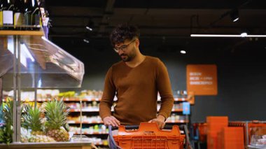 Alışveriş arabalı bir Arap süpermarket sebze reyonundan taze indirimli ananas seçiyor. Etrafı tropik meyve ve sebzelerle çevrili..