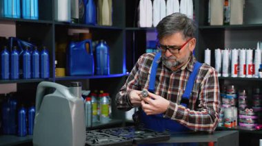 Deneyimli erkek oto yedek parça satıcısı, çevresi yağ kapları ve mekanik malzemelerle çevrili bir atölyede otomotiv araçları düzenliyor..