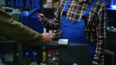 Üst düzey bir oto yedek parça mağazasından motor yağı alırken, terminalde ulaşılamayan ödemeler için akıllı telefon kullanan bir müşterinin yakın plan fotoğrafı..