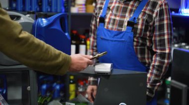 Bir otomobil parçası perakende ortamında motor yağı alırken, bir terminalde kontak kurulamayan ödemeler için akıllı telefon kullanan müşterinin el çekimi.
