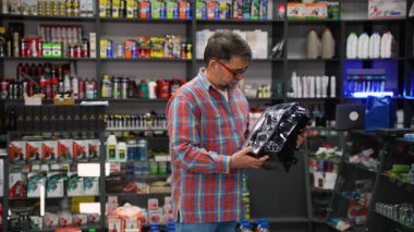 Ekose gömlekli yaşlı bir adam oto yedek parça dükkanında yeni bir araba farını inceler, satın almadan önce aracının uyumluluğunu kontrol eder..