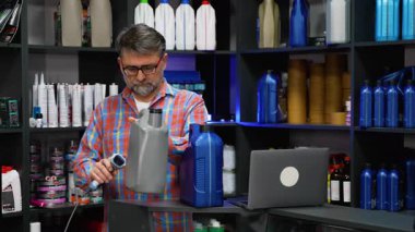 Olgun erkek çalışanlar, iyi organize edilmiş otomobil parçaları satan bir mağazada envanter kontrolü sırasında motor yağı şişesindeki barkodları tarıyor..