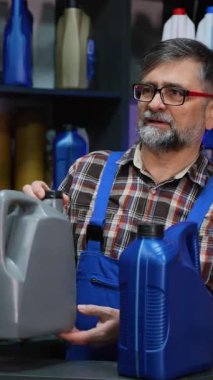 Ekose gömlekli ve mavi tulumlu deneyimli bir erkek kâtip müşterinin motor yağı seçmesine yardımcı olur ve otomobil yedek parça mağazasında ürün detaylarını açıklar..