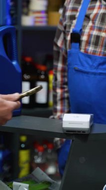 Bir otomobil parçası perakende ortamında motor yağı alırken, bir terminalde kontak kurulamayan ödemeler için akıllı telefon kullanan müşterinin el çekimi.