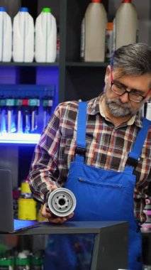 Üst düzey erkek oto yedek parça satıcısı, bir dizüstü bilgisayar ve ürün raflarının yanındaki tezgahta barkod okuyucu kullanarak silindirik bir araba yağı filtresi tarıyor..