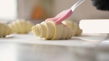 Şef pişmemiş kruvasan ile parşömen kağıdına yumurta yıkar, profesyonel bir mutfak ortamında pişirmek için hazırlar..