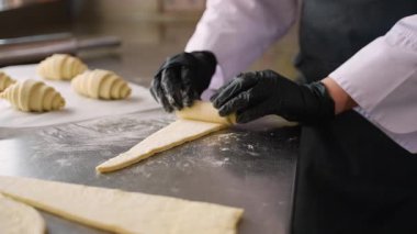 Eldivenli profesyonel şefin yakın plan çekimi kruvasan hamuru, paslanmaz çelik yüzey ve fırın mutfağında un ile elle sarması..