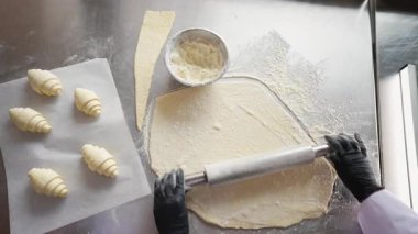 Bir şefin, kruvasan hamurunu hamur tezgahında hamur işi ve hamur işi ve un kasesinin yanında düzleştirmek için merdane iğne kullanışının yukarıdan görünüşü..