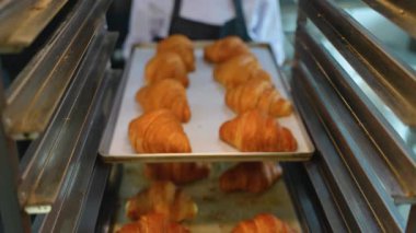 Baker, ticari bir mutfakta pişirdikten sonra serinletmek için metal bir rafın üzerine bir tepsi altın kruvasan koyar..