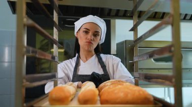 Şef üniformalı oyuncu kadın, sıcak bir pastanede taze pişmiş altın kruvasan sunarken sevinçle şarkı söylüyor..