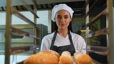 Üniformalı kadın fırıncı gururla sunar yeni pişmiş baget ve yuvarlak somunları profesyonel bir fırın mutfağında tepside sunar.