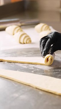 Profesyonel şef dikkatli bir şekilde üçgen hamuru kruvasana çeviriyor. Yanında hamur işleri olan bir fırın mutfağında un metal bir yüzey üzerinde..