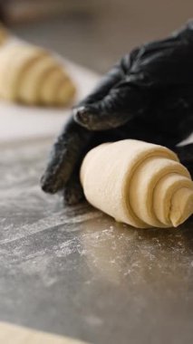 Bir fırın mutfağında, paslanmaz çelik bir yüzey üzerinde kruvasan hamurunun rulosunu dikkatlice bitiren, eldivenli şeflerin yakın çekimi..