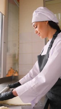 Üniformalı kadın fırıncı ve eldivenli fırın mutfağında taze kruvasan hazırlarken metal bir yüzeye iğneyle hamur atıyor..