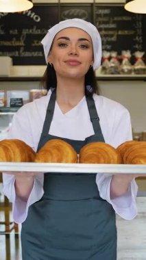 Şef üniformalı genç bir kadın sıcak bir pastanenin içinde gururla gülümserken elinde bir tepsi dolusu yeni pişmiş kruvasan tutuyor..