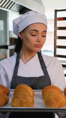 Şef üniformalı oyuncu kadın, sıcak bir pastanede taze pişmiş altın kruvasan sunarken sevinçle şarkı söylüyor..