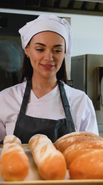 Üniformalı kadın fırıncı profesyonel bir fırın mutfağındaki metal bir rafta serinlemek için dikkatlice bir somun ekmek bırakıyor..