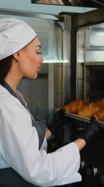 Üniformalı profesyonel kadın fırıncı bir fırının mutfağından bir tepsi altın, kabuklu ekmek alıyor..