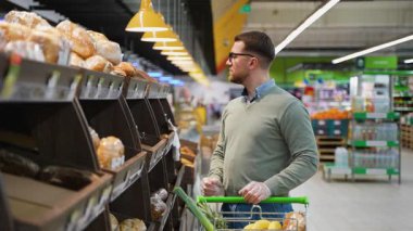 Bir adam markette alışveriş yaparken fırın bölümünden taze ekmek seçiyor..