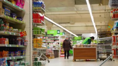 Yeşil süveter ve gözlüklü bir adam marketin taze meyve reyonuna bakarken muz, marul ve ekmekle dolu bir alışveriş arabasını itiyor..