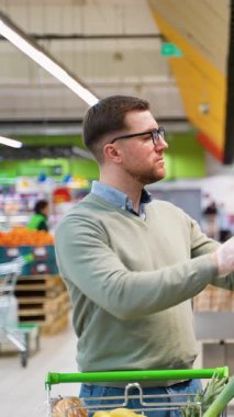 Bir adam süpermarketteki fırın bölümünden taze ekmek toplarken içi alışveriş arabasıyla dolu bir alışveriş arabasını itiyor..