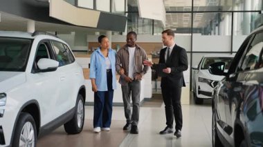 Mutlu Afro-Amerikan çifti araba galerisinden yeni bir araba seçiyor. Danışman farklı seçenekleri ve özellikleri tartışıyor.