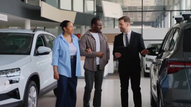 Modern araba galerisinde yeni araç seçeneklerini araştıran Afrikalı Amerikalı çift. Potansiyel satın alma konusunda satış uzmanıyla görüşüyorum. Heyecanla ve paylaşılan heyecanla otomobili incelemek