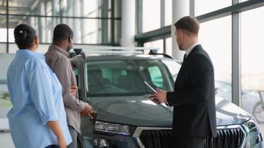 Afrika kökenli Amerikalı çifte yeni araba özellikleri gösteren profesyonel bir satıcı modern bir galeride doğru aracı seçmelerine yardım ederek mükemmel müşteri hizmetleri sunuyor.