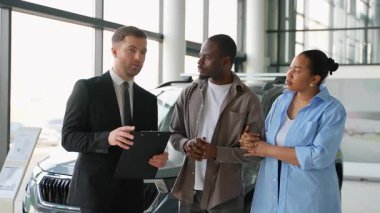 Afro-Amerikan bir çifte yeni araçlar sunan profesyonel bir araba satıcısı bayilikte bilgilendirilmiş bir seçim yapmalarına yardımcı oluyor.