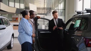 Araba galerisinde Afro-Amerikan bir çifte yeni bir arabanın özelliklerini gösteren profesyonel bir araba satıcısı, onlara bilinçli bir karar vermelerinde yardımcı oluyor.