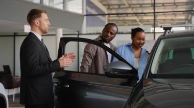 Afro-Amerikan bir çifte yeni bir arabanın özelliklerini gösteren profesyonel bir araba satıcısı bilinçli bir karar vermelerine yardımcı oluyor.