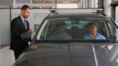 Araba satıcısı Afrika kökenli Amerikalı çifte araç özelliklerini açıklıyor, iç detayları inceliyor ve satış danışmanlığı sırasında otomotiv seçeneklerini tartışıyor.