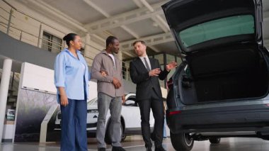 Profesyonel bir araba satıcısı, yeni bir arabanın bagajını bir araba galerisinde Afro-Amerikan bir çifte gösteriyor. Bilinçli bir karar vermelerine yardımcı oluyor.