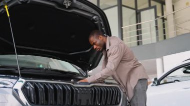 Potansiyel alıcı, satın alma kararı vermeden önce, bir galeride yeni bir arabanın motor bölmesini dikkatle inceler ve detaylara olan ilgisini gösterir.