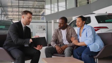 Profesyonel araba satıcısı Afrika kökenli Amerikalı çifte önemli bir satış sözleşmesi sunuyor. Çağdaş galeride araç seçimine rehberlik ediyor.