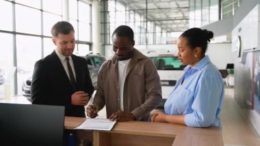 Profesyonel araba satıcısı, Afrikalı Amerikalı çifte evrak işlerinde yardım ediyor ve modern araba galerisindeki yeni arabalarının anahtarlarını teslim ediyor.