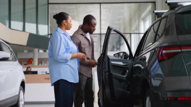 Satış danışmanı Afro-Amerikan çiftin galeride yeni araba seçmesine yardım ediyor. Satın almadan önce özellikleri ve seçenekleri tartışıyorlar.