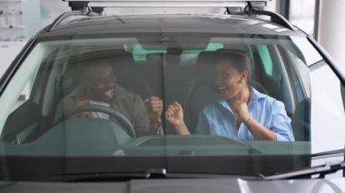 Mutlu müşteriler, Afrikalı bir Amerikalı erkek ve kadın, yeni bir arabada oturuyor, test ediyor ve seçiyor, ellerini hareket ettiriyor ve olumlu duygularını ifade ediyorlar.