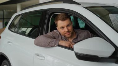 İçeride oturan hevesli alıcı yakın zamanda beyaz bir araç satın aldı, araba anahtarlarını tutuyor ve modern galeride otomotiv sahibi olmayı kutlarken gülümsüyor.