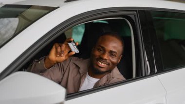 Gururlu Afro-Amerikan müşteri yeni araba mülkiyetinin keyfini çıkarıyor, galerinin içinde araba anahtarı sergilenirken gülümsüyor.