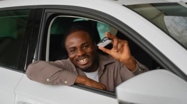 Afrika kökenli Amerikalı erkek yeni araba alımını kutluyor, araba anahtarlarını gururla sergiliyor ve galeride büyük başarılar sergiliyor, neşe ve başarıyı ifade ediyor.