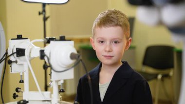 Gelişmiş tıp teknolojisinin yanında kendine güvenen genç bir çocuk, temiz laboratuvar ortamında parlak bir gülümsemeyle olumlu bir jest sergiliyor.