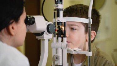 Optometrist, göz hekiminde, bir göz hastalıkları ve görme bozukluklarını kontrol etmek için, kesik lamba ile biyomikroskop kullanan genç bir çocuğun gözlerini inceliyor.