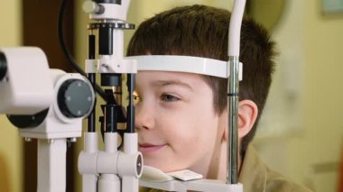 Genç çocuk, bir yarık lamba kullanılarak kapsamlı bir göz muayenesinden geçiyor. Bu da çocuklarda göz sağlığı değerlendirmesi sürecini gösteriyor.