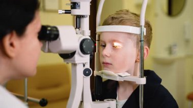 Profesyonel tıbbi klinik ortamında yarık lamba teşhis aleti kullanarak genç hastaların göz sağlığını inceleyen yetenekli bir optometrist.