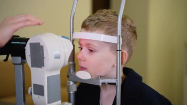 Doktor, otomatik fraktör kullanan küçük bir çocuğu görme kontrolü yapıyor. Kırılma hatasını ölçmek ve gözlük reçetesini belirlemek için bir cihaz.